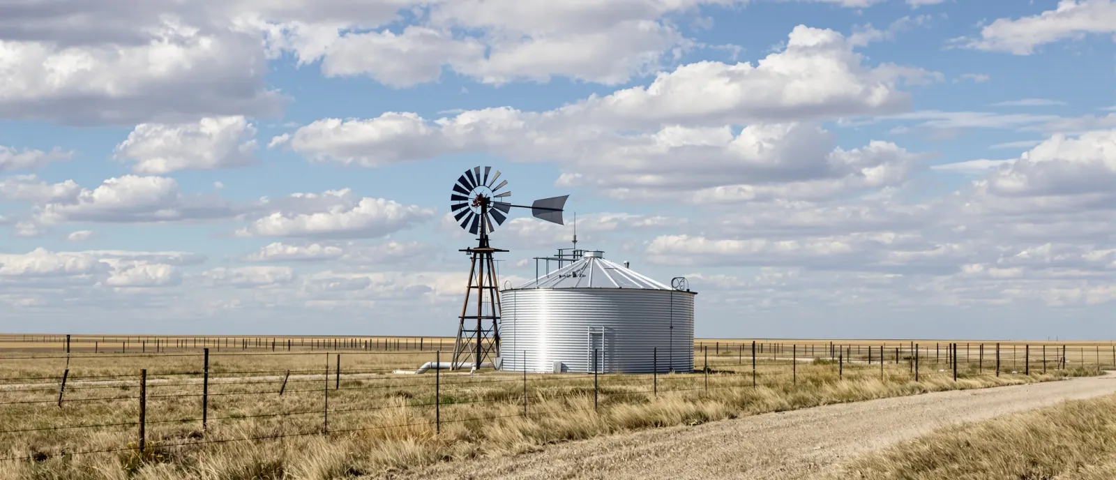 A galvanised stock tank and windmill water pump in a fenced pasture on the Great Plains