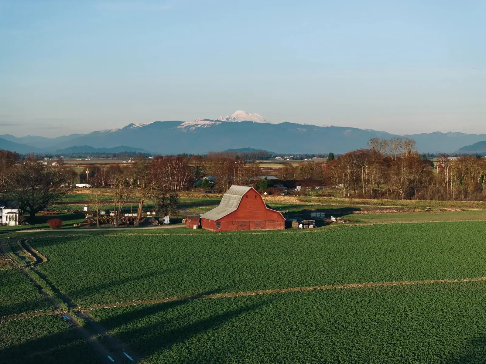 Aerial view of a red barn beside a broad green field on a Pacific Northwest farm, with a snow-capped mountain on the horizon.