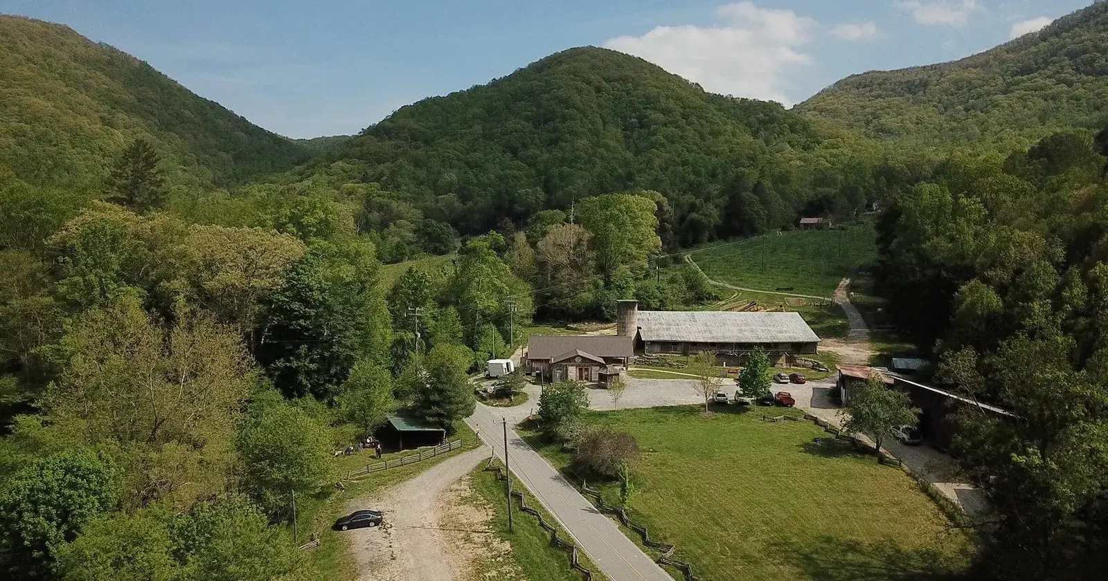 Hickory Nut Gap Farm: Aerial view of the farm buildings, barn and pastures nestled among wooded mountains.