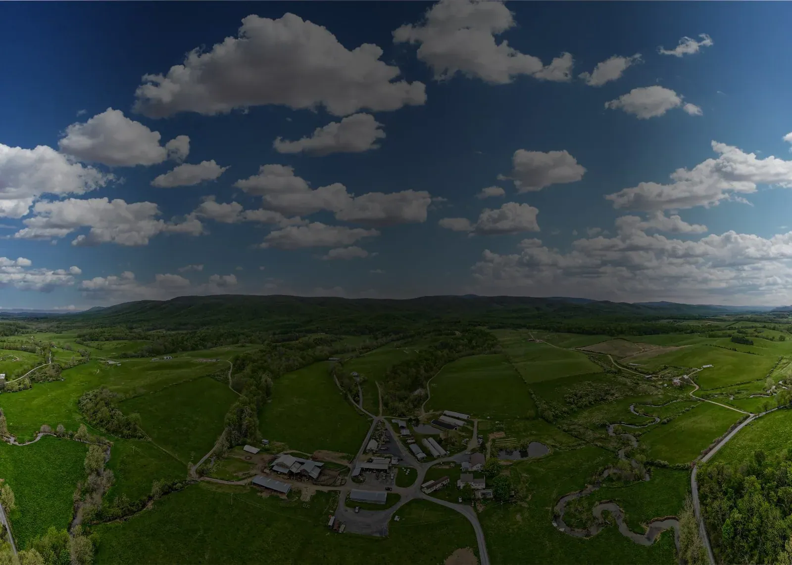 Polyface Farms: Aerial view of the Polyface farmstead and its green pastures in the Shenandoah Valley under a cloudy sky (banner image, slightly darkened at the top).