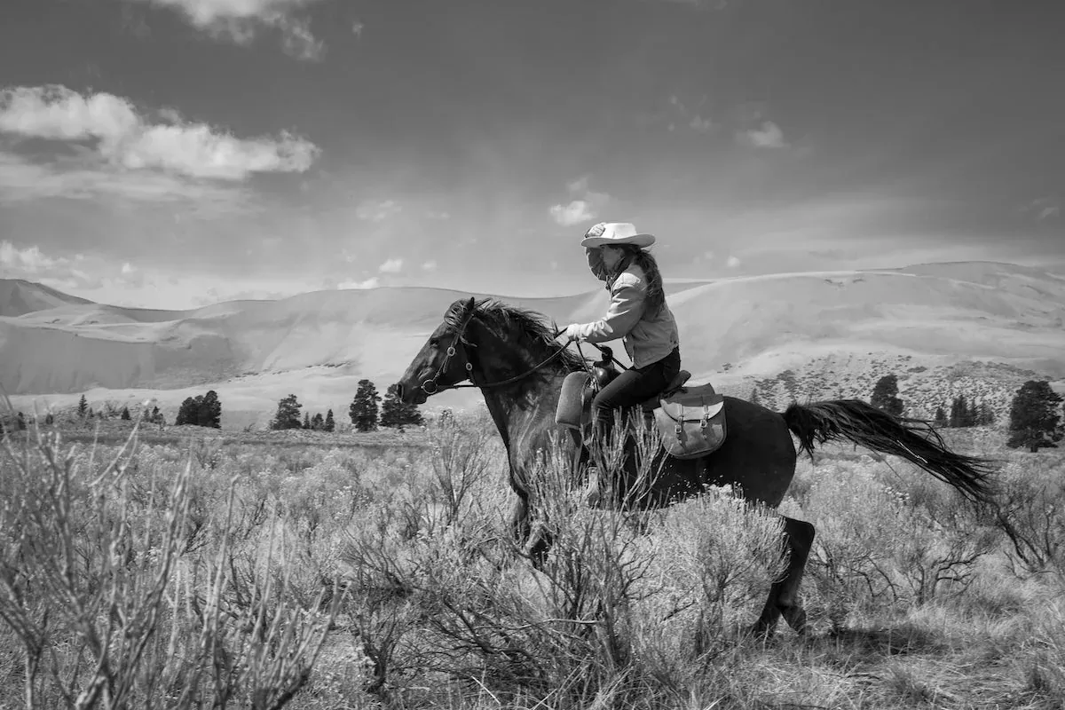 Ranchlands: Black-and-white shot of a rider loping a horse through sagebrush at Zapata Ranch, with the sand dunes behind.