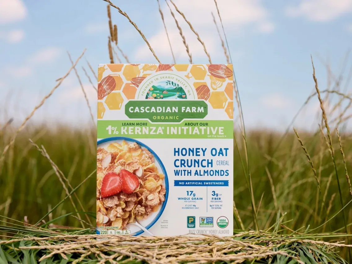General Mills: A box of General Mills' Cascadian Farm Organic Honey Oat Crunch cereal with the 1% Kernza Initiative banner standing in a field of ripe Kernza perennial grain.