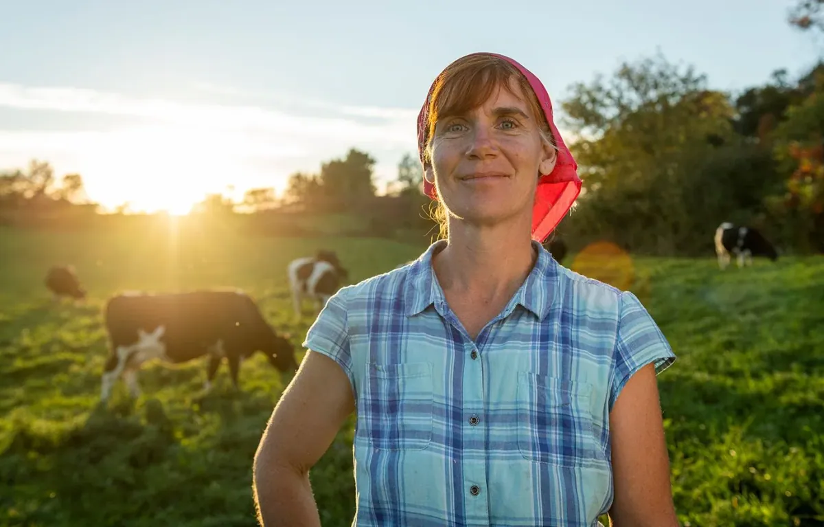 Organic Valley: Organic Valley farmer Christianson standing in a sunlit pasture with grazing Holstein cows behind her.