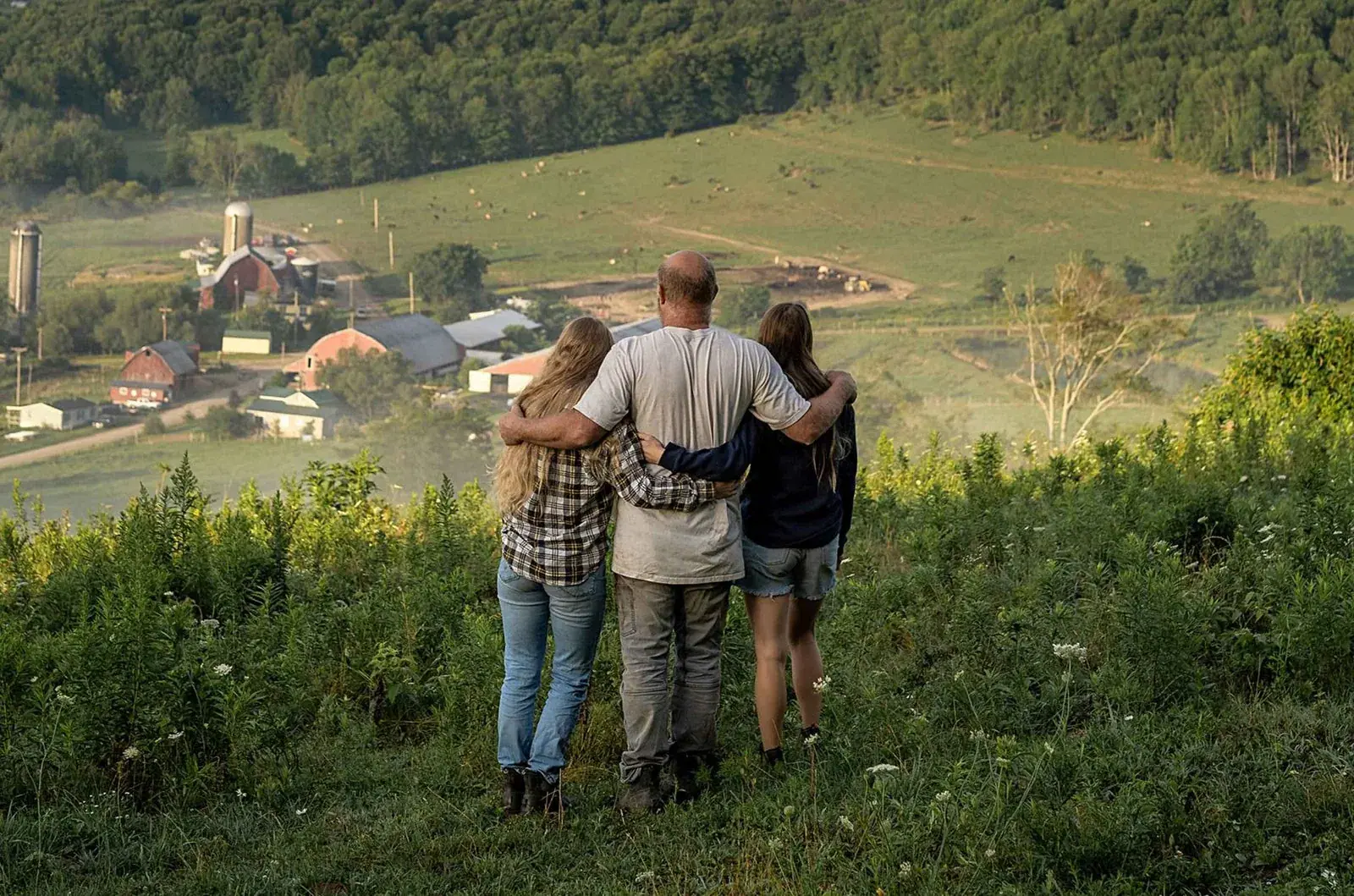 Painterland Sisters: The Painter family standing arm in arm on a hillside, looking down over their Pennsylvania dairy farm with red barns, silos and pastures.