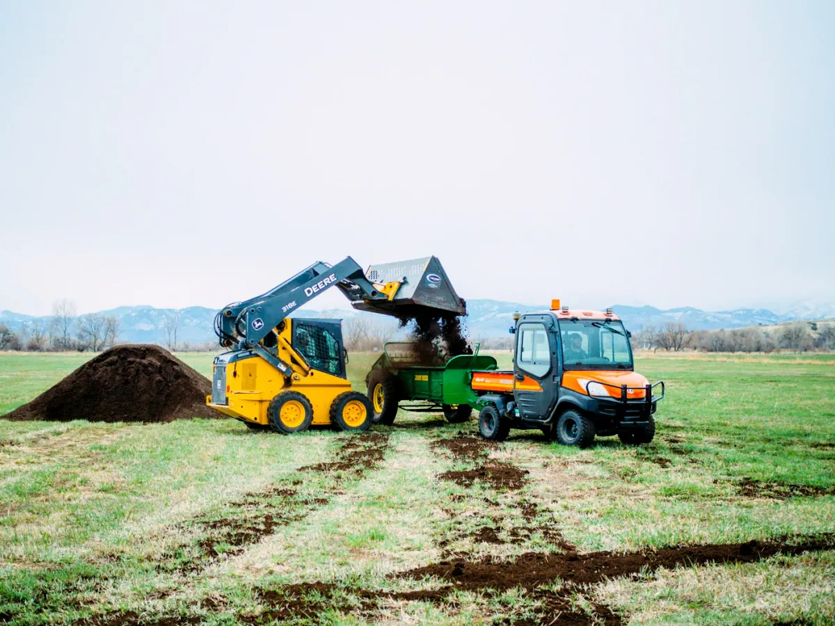 Zero Foodprint: A skid-steer loader fills a compost spreader from a compost pile on the pasture of a Zero Foodprint farm grantee in Colorado, with fresh compost strips on the grass.