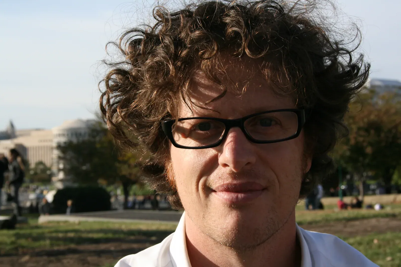 Peter Byck: Close portrait of Peter Byck with curly hair and dark-rimmed glasses outdoors, the US Capitol area blurred behind him (an older press photo from the Carbon Nation release).