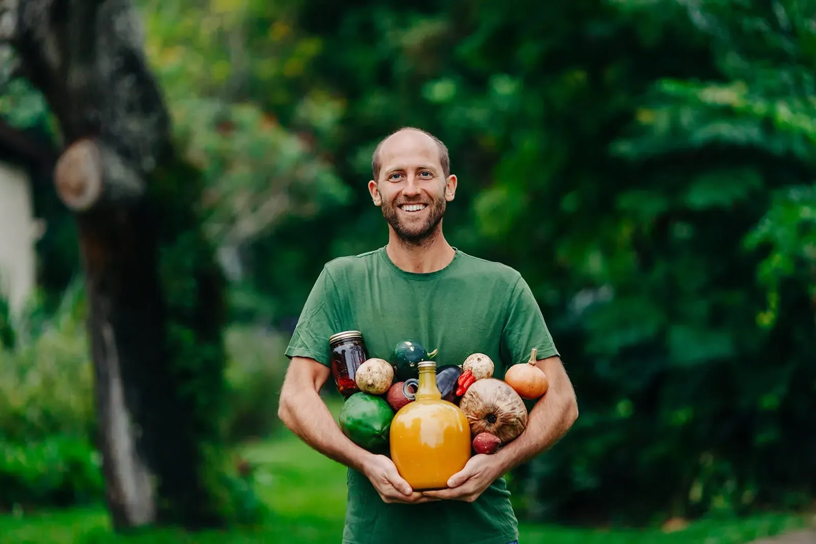 Robin Greenfield: Robin Greenfield smiling in a garden holding an armful of homegrown and foraged food, jars and squash; the hero photo of his official site, which dedicates its photos to the public domain (CC0).