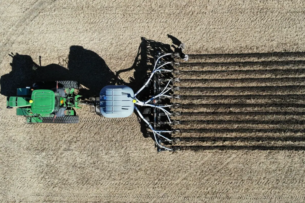 Dawn Equipment: Top-down drone view of a tractor pulling a toolbar of Dawn Pluribus row units with a front tank, building strips in a residue-covered field.