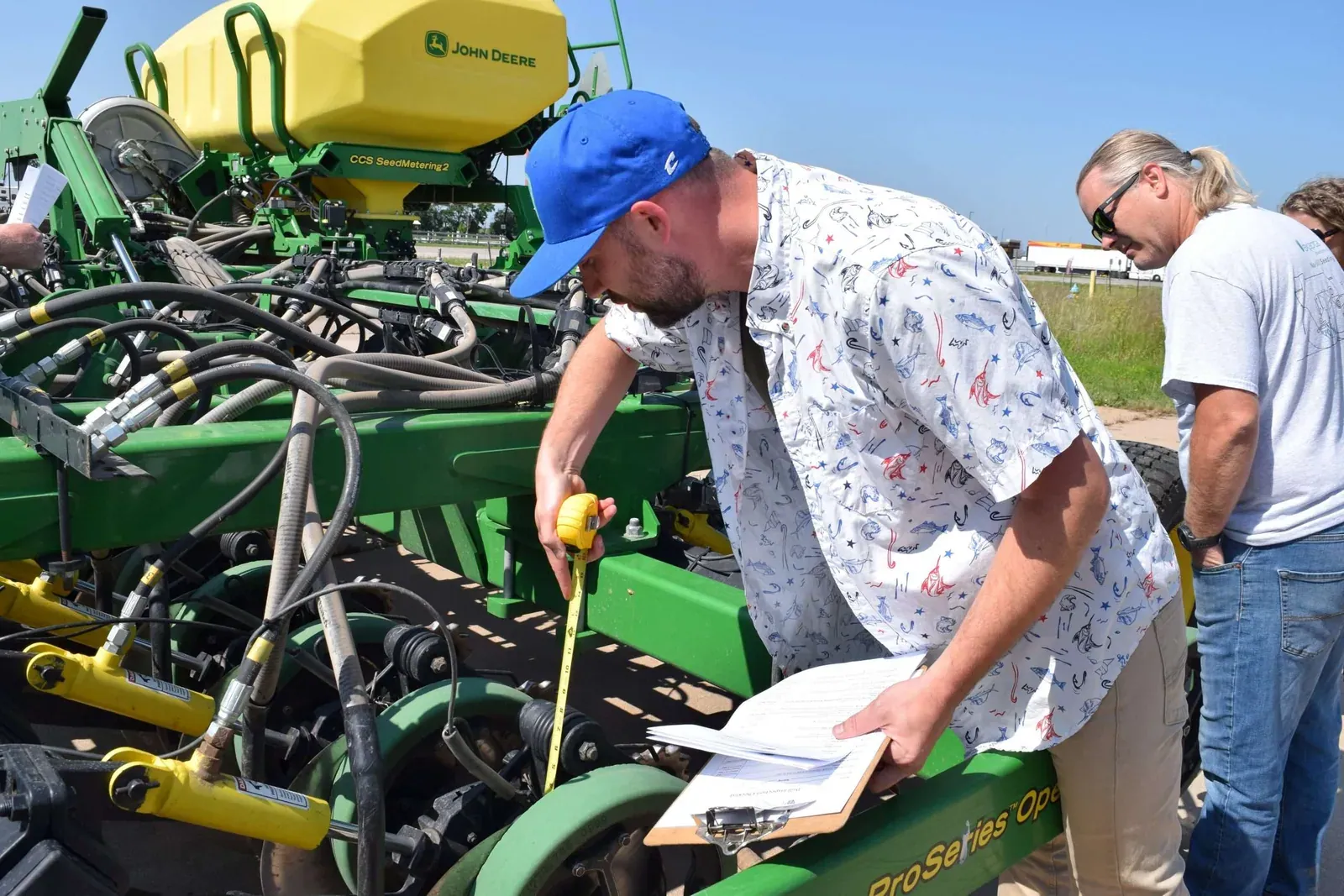 Exapta Solutions: An Exapta staff member measures the row units of a John Deere seeding implement with a tape measure and clipboard during a drill inspection.
