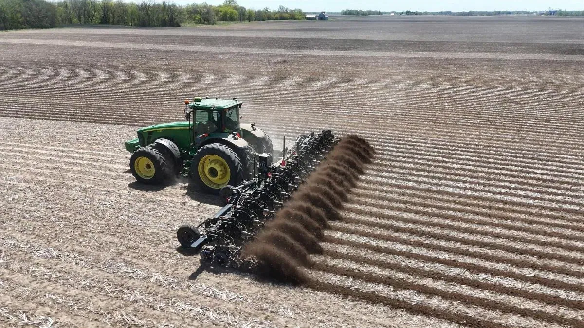 Yetter Farm Equipment: Aerial view of a tractor pulling a Yetter strip-till toolbar across a field, each row unit throwing up a plume of soil.